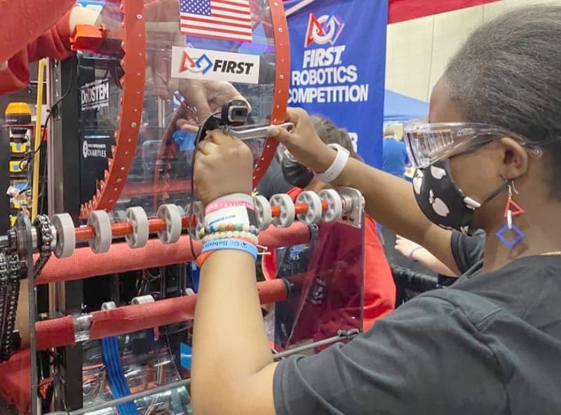 Tobi in safety glasses, working on a robot's drivetrain at the FIRST Robotics Competition.