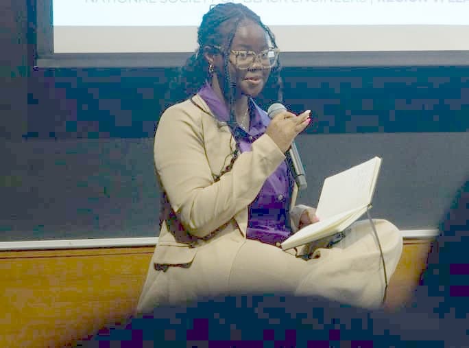 Tobi speaking into a microphone, hosting a panel at the NSBE Region VI Leadership Conference.